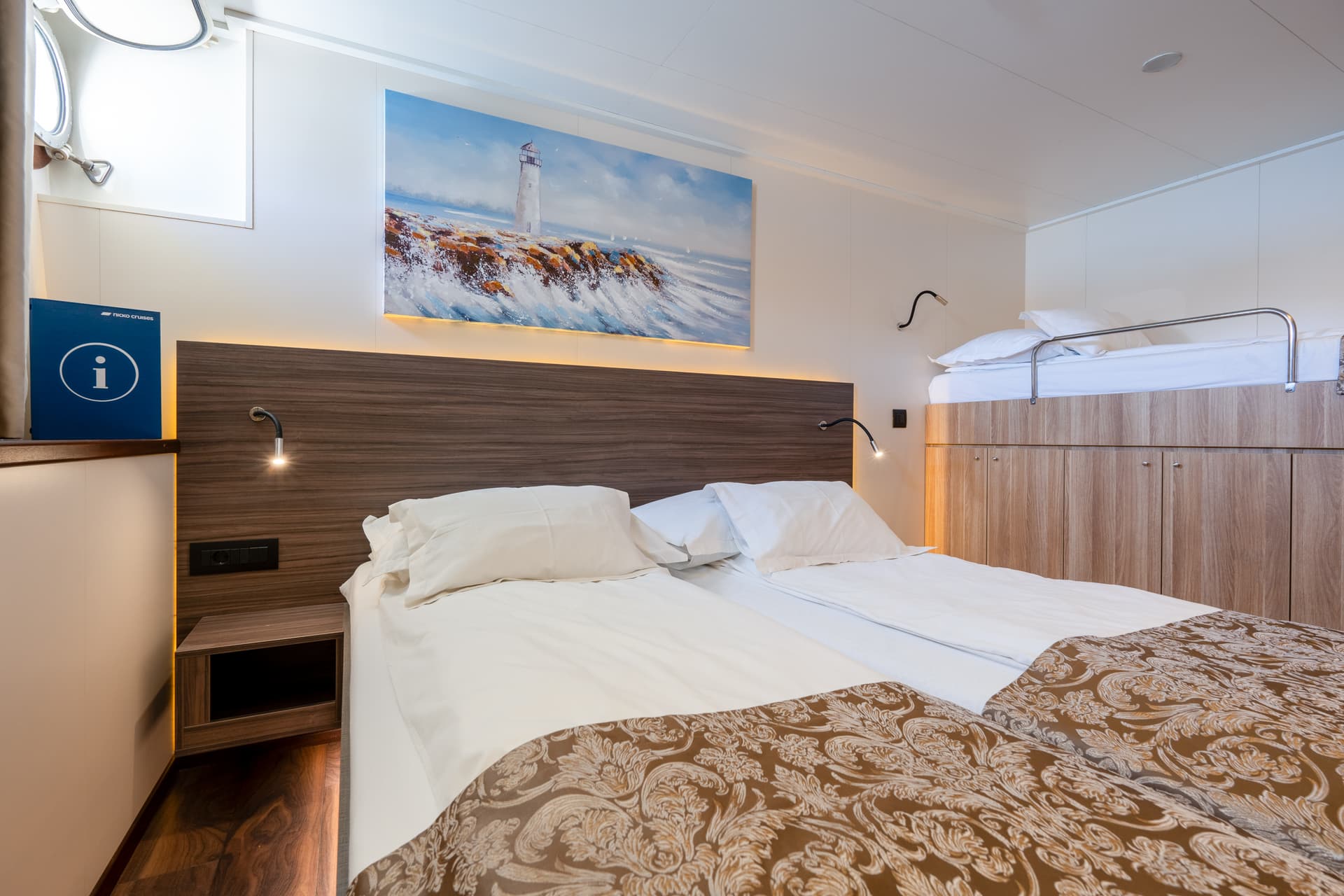 Standard deck cabin interior with twin beds and lighthouse wall art