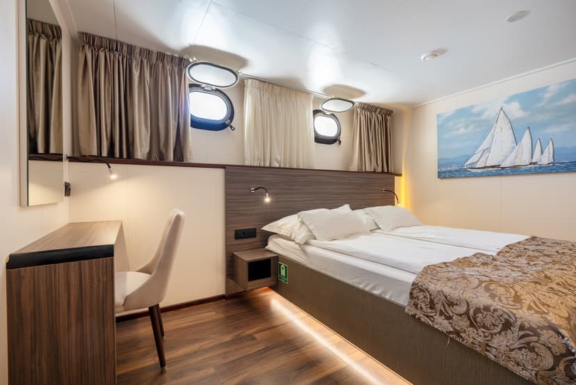 Standard ship cabin with double bed, desk, and porthole windows