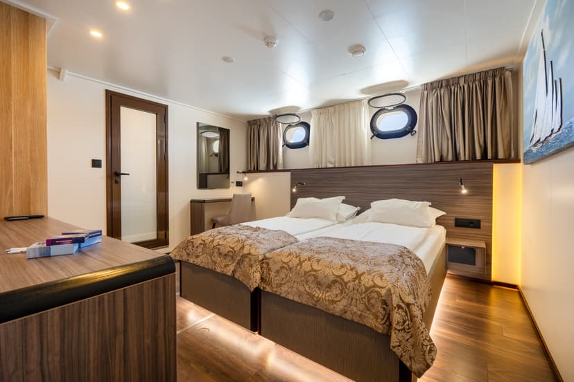 Standard deck cabin with two twin beds, porthole windows, and wooden furnishings on a cruise ship.