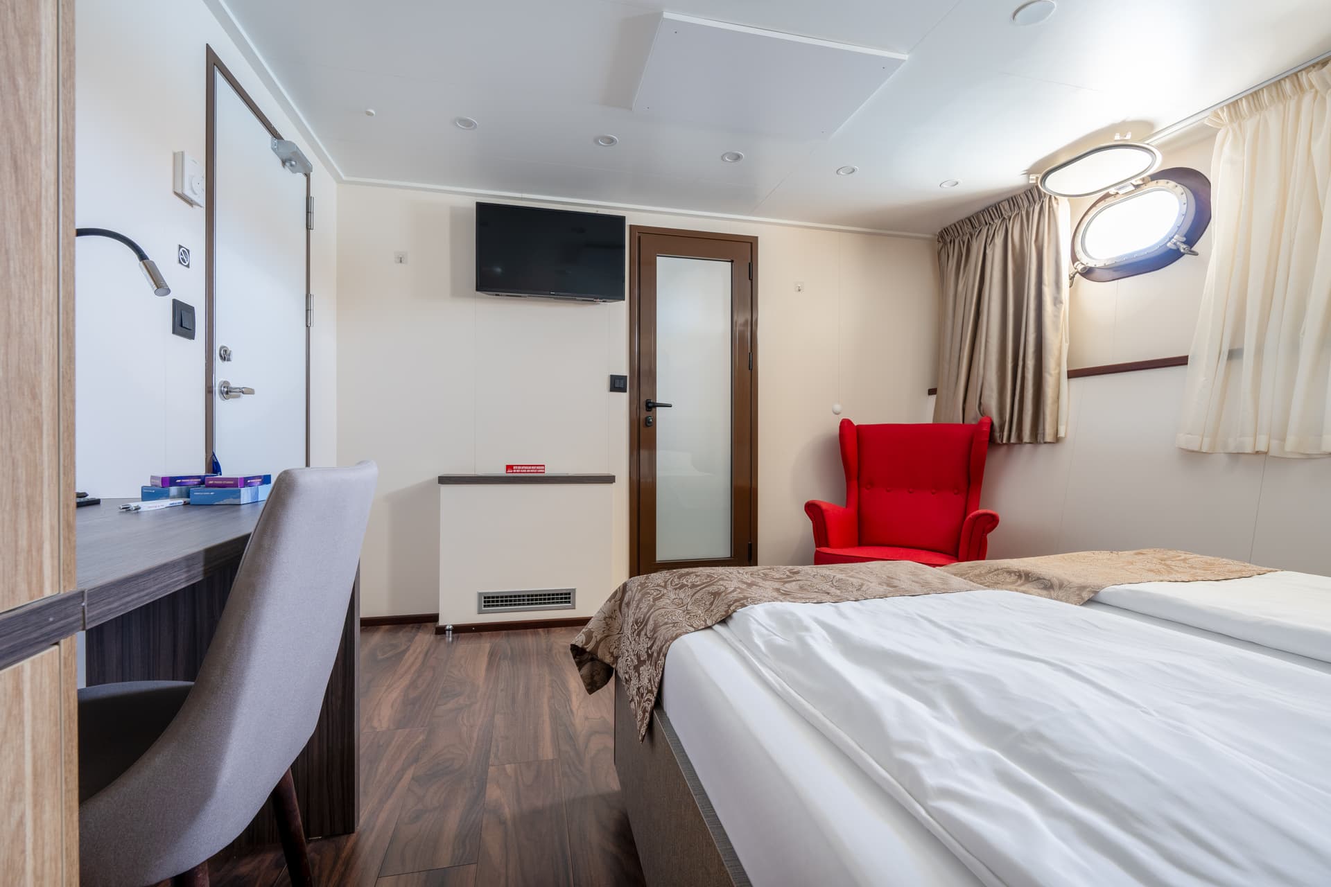 Standard cruise ship cabin interior with bed, desk, and red armchair