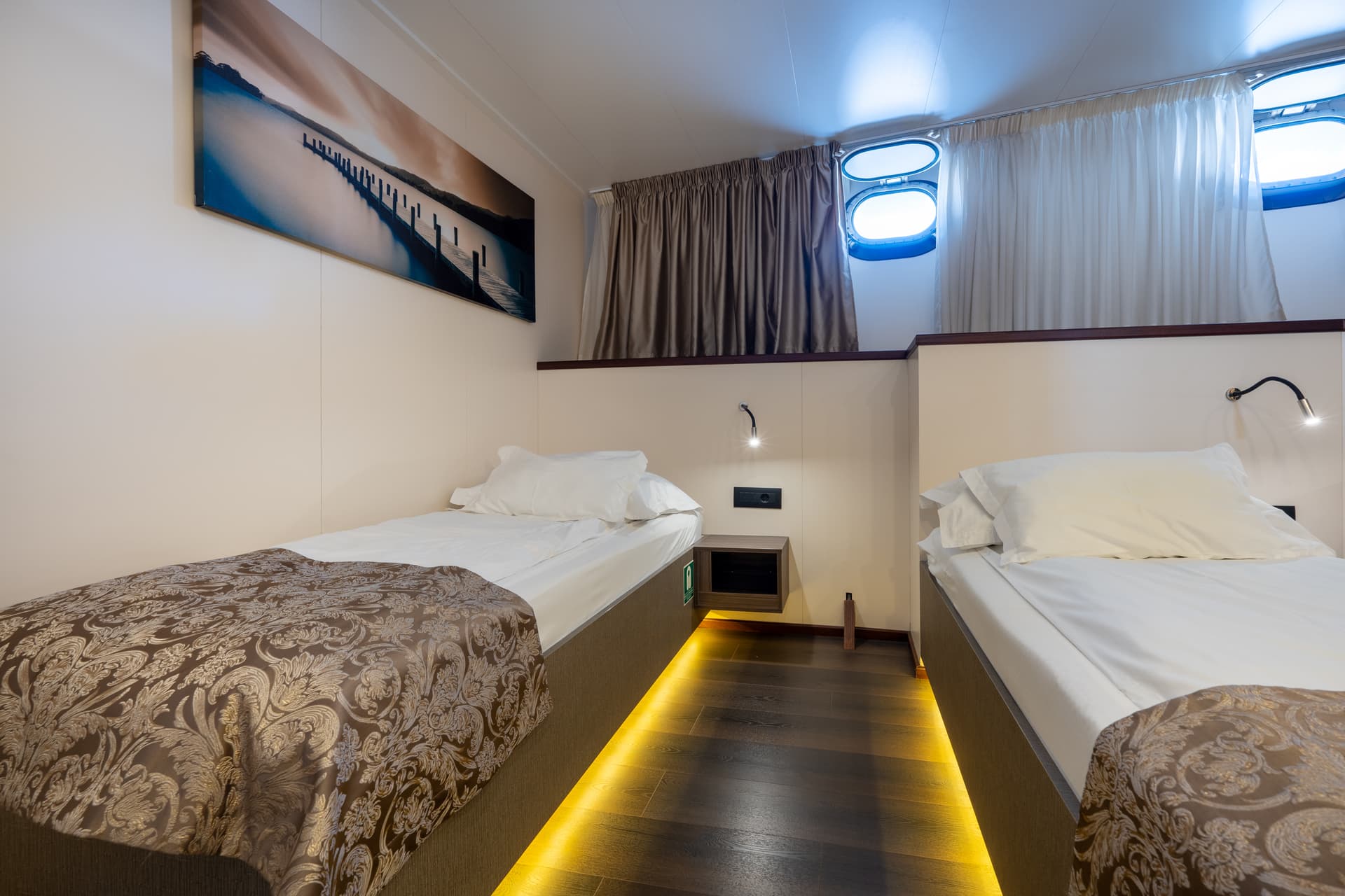 Standard ship cabin with two twin beds, portholes, and wall art.