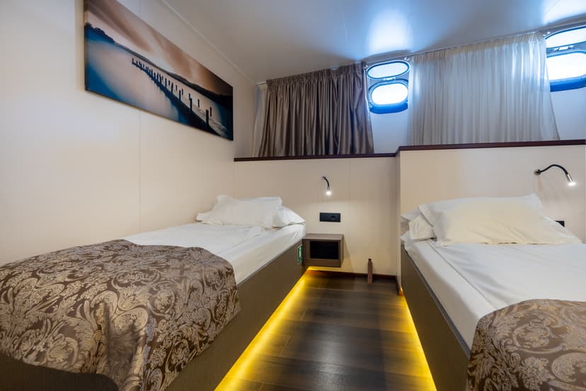 Standard ship cabin with two twin beds, portholes, and wall art.
