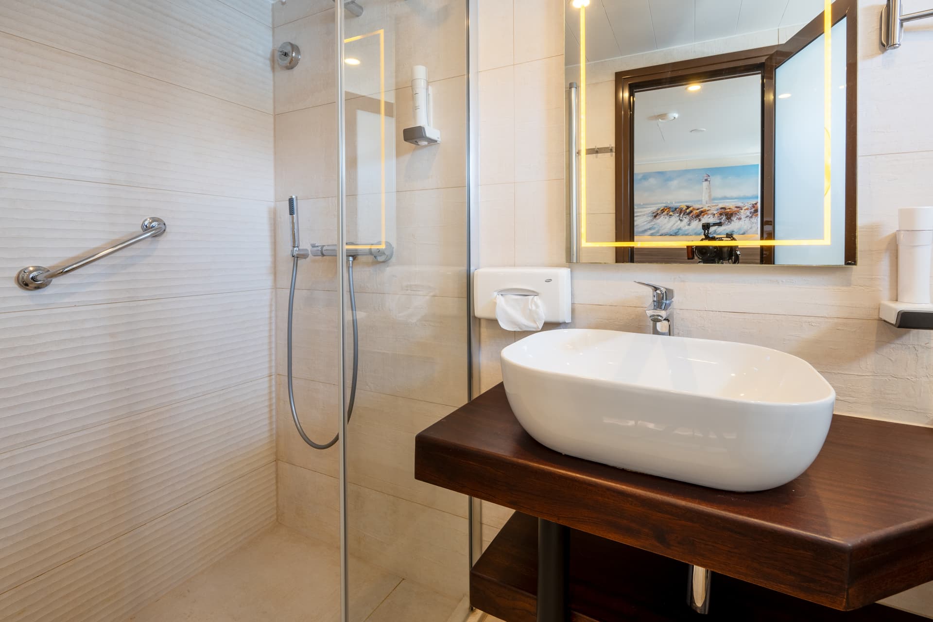 Modern hotel bathroom with white vessel sink, wooden vanity, and glass shower enclosure