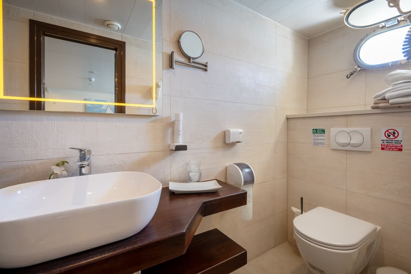 Modern bathroom interior with white vessel sink, dark wood countertop, toilet, and porthole window