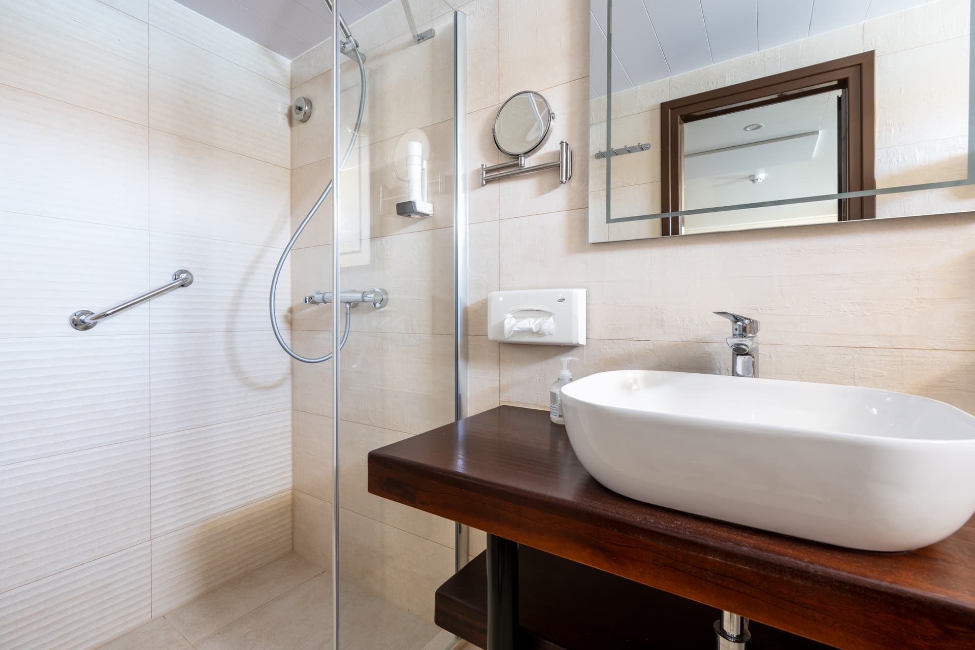 Modern hotel bathroom with white vessel sink, wooden vanity, and glass shower enclosure