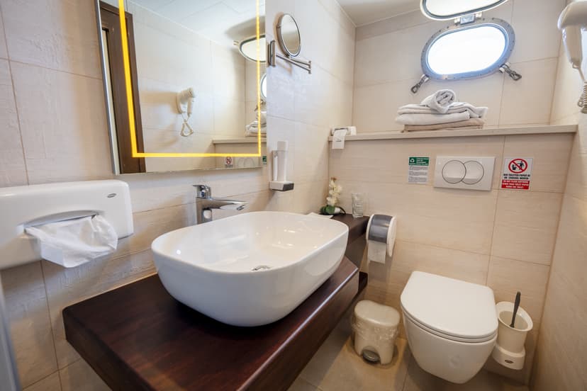 Modern compact bathroom with vessel sink, illuminated mirror, toilet, and porthole window