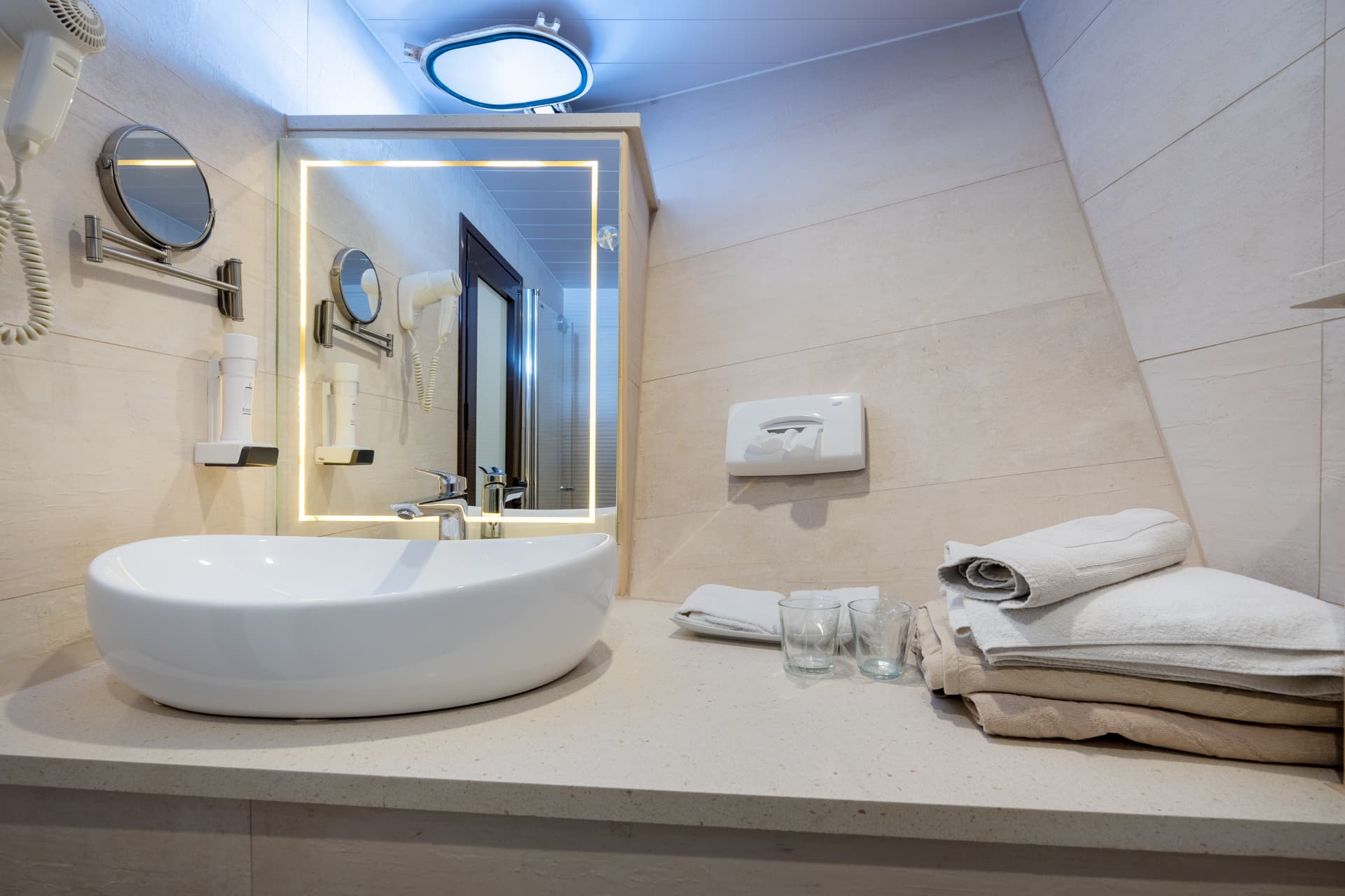 Modern bathroom vanity with white vessel sink, backlit mirror, and folded towels