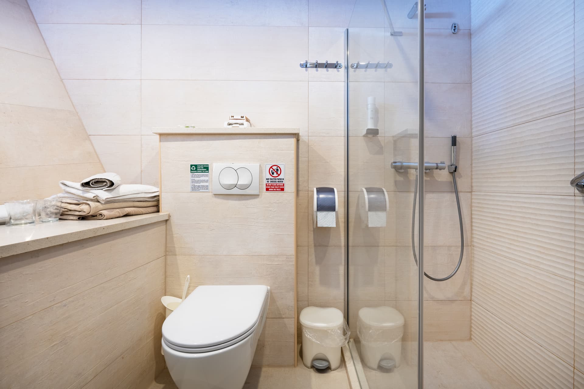 Modern hotel bathroom with white toilet, glass shower enclosure, and stacked towels on counter