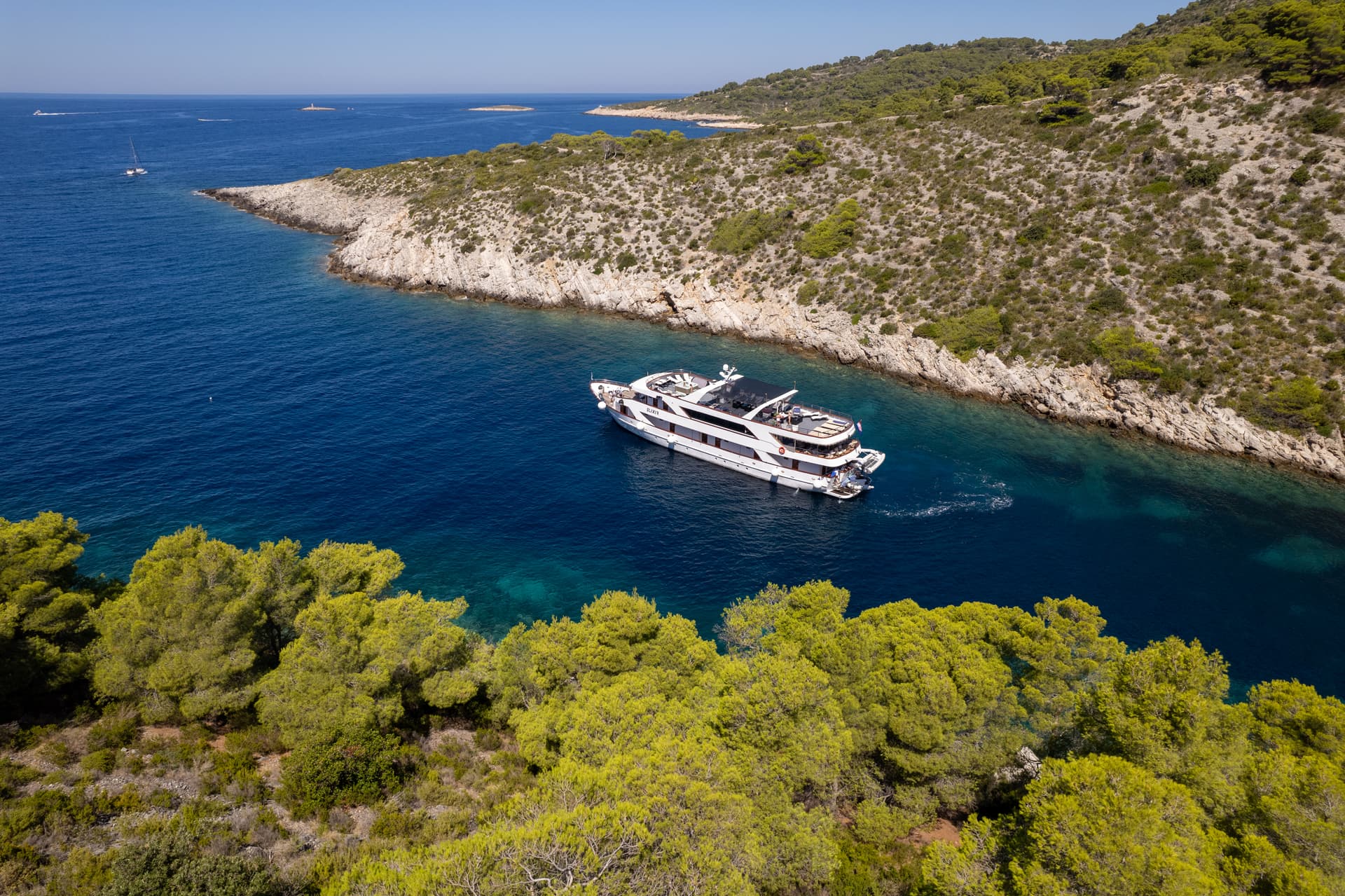 Yacht anchored in a coastal cove with green pine trees and blue sea water