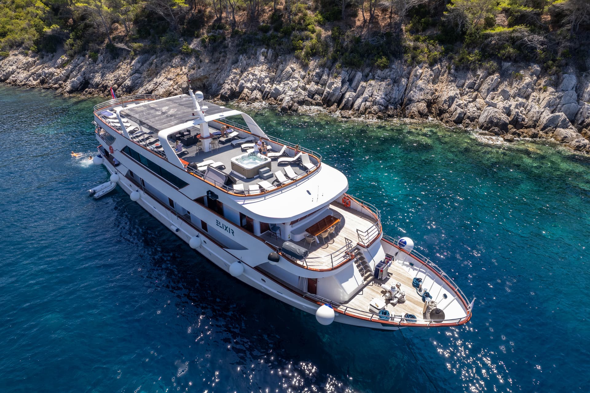 Large yacht anchored in crystal clear coastal waters near rocky shoreline