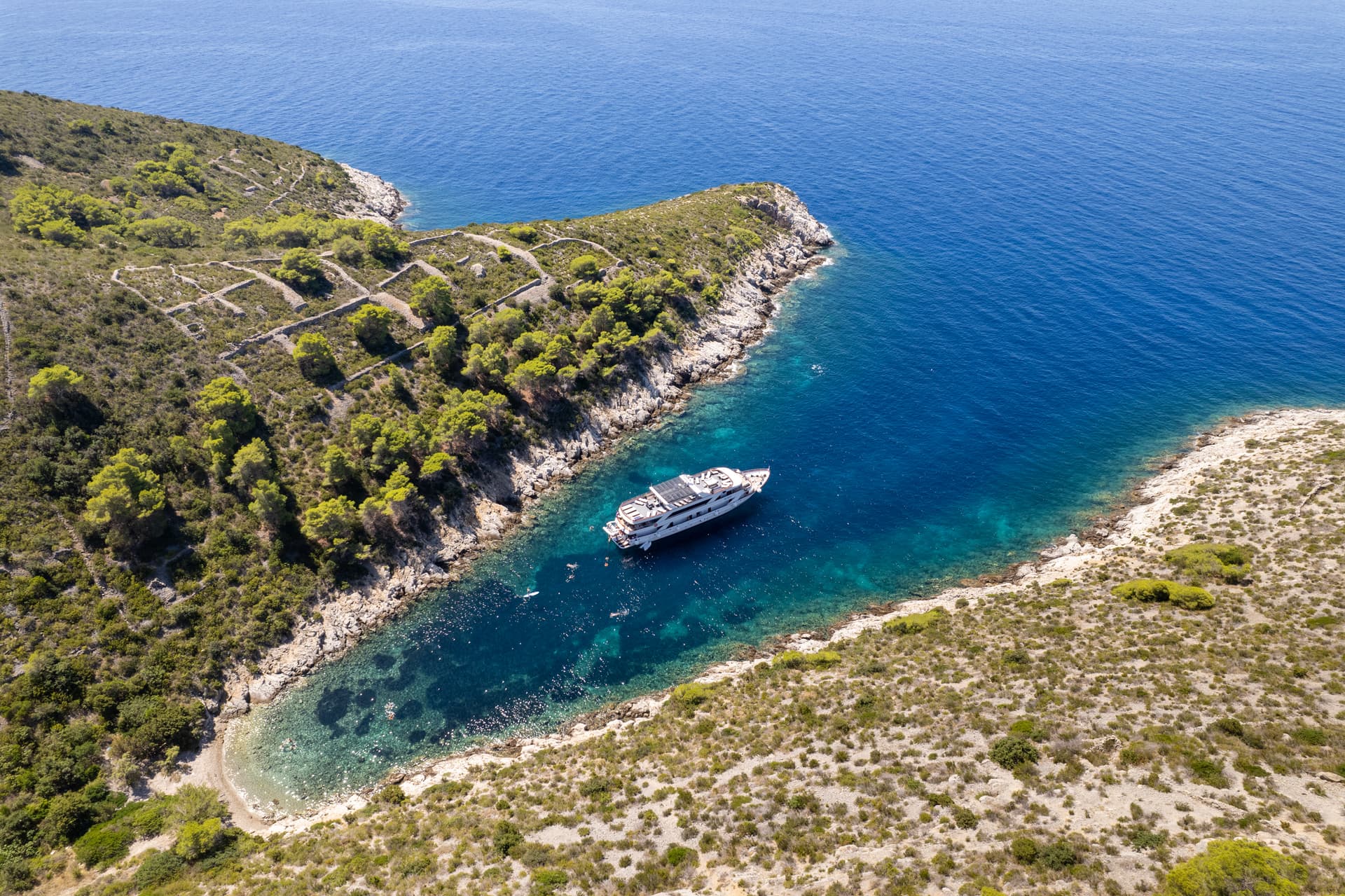 Yacht anchored in a secluded cove along a rocky coastline with blue sea water