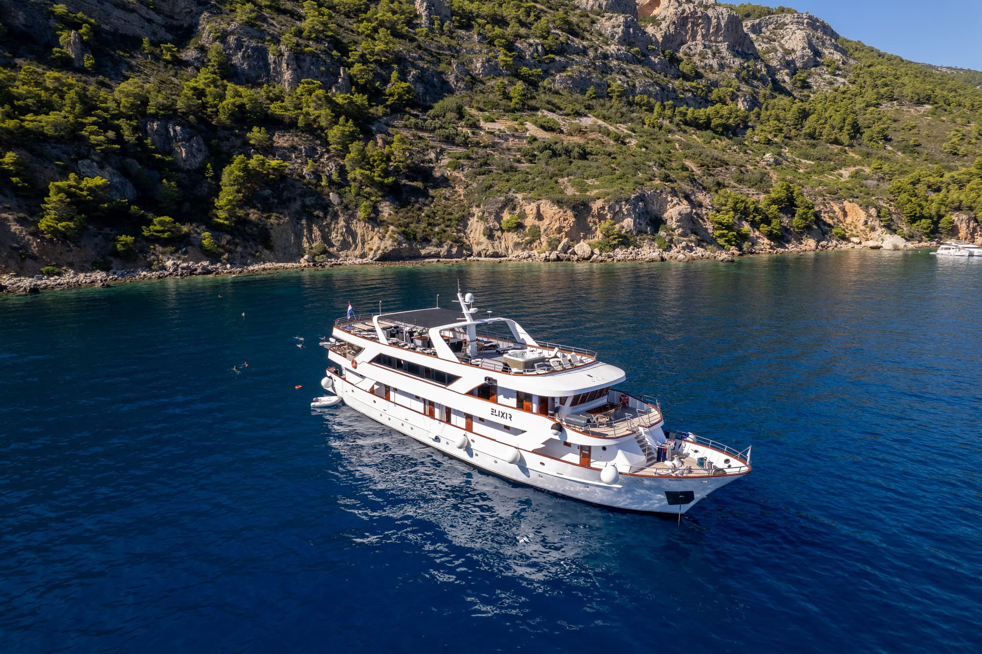 Luxury yacht anchored in a blue coastal bay near a wooded hillside