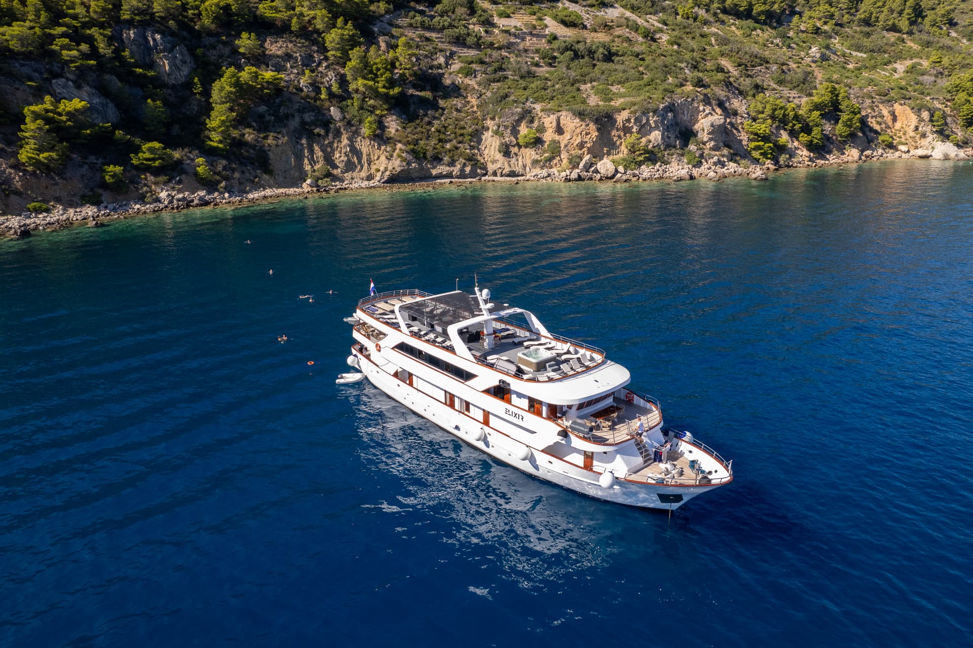 Large white yacht on blue coastal waters near a rocky shoreline
