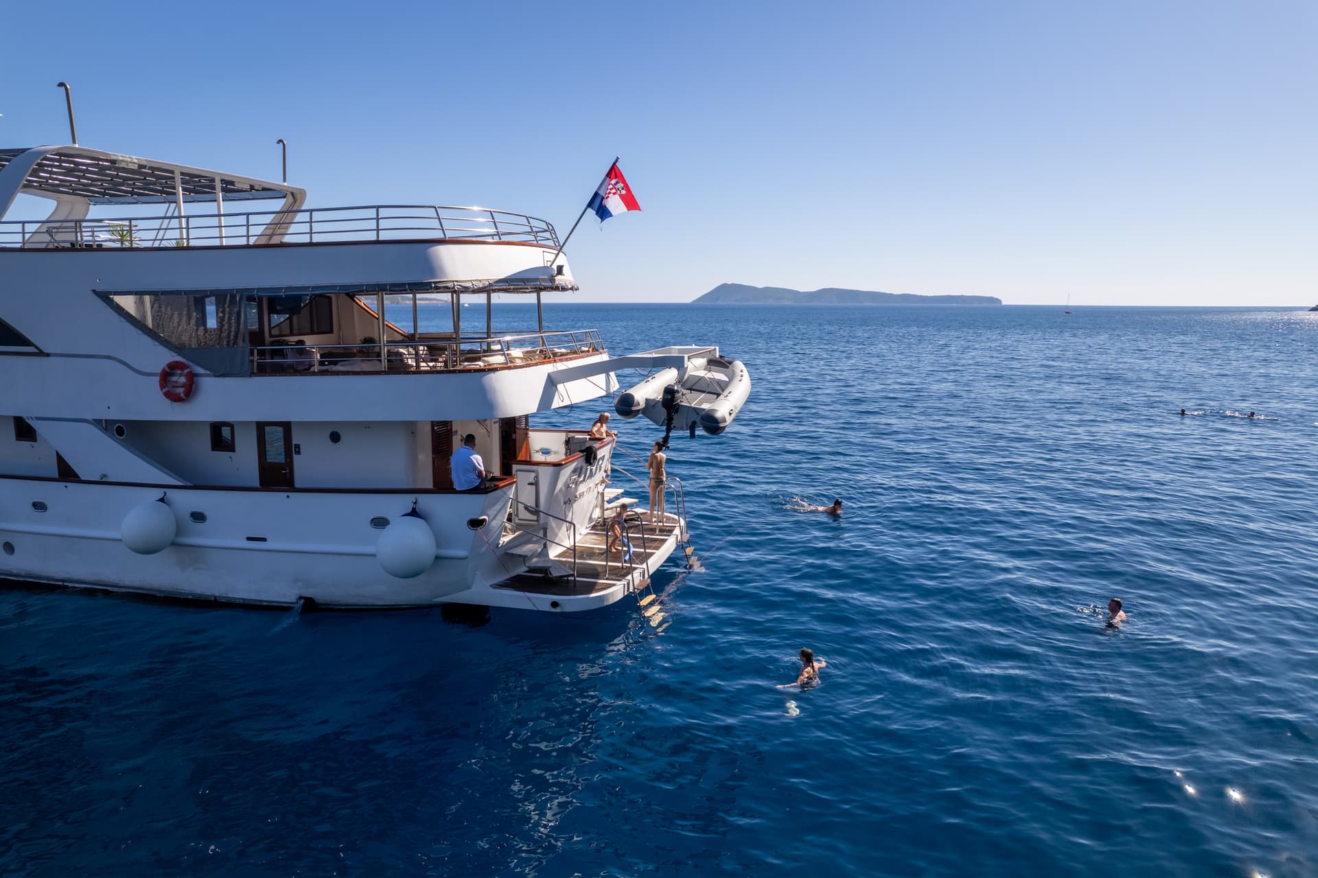 Large white yacht on blue sea with people swimming in the water
