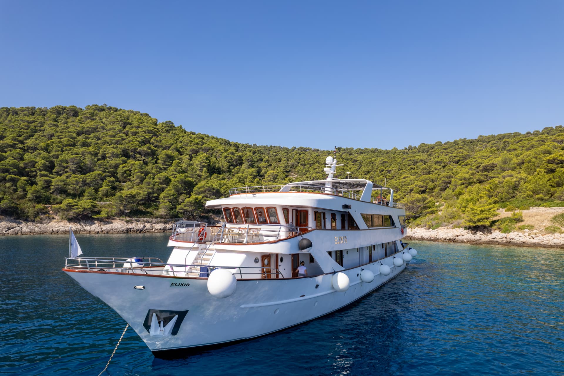 White yacht anchored in a coastal bay with green forested hills