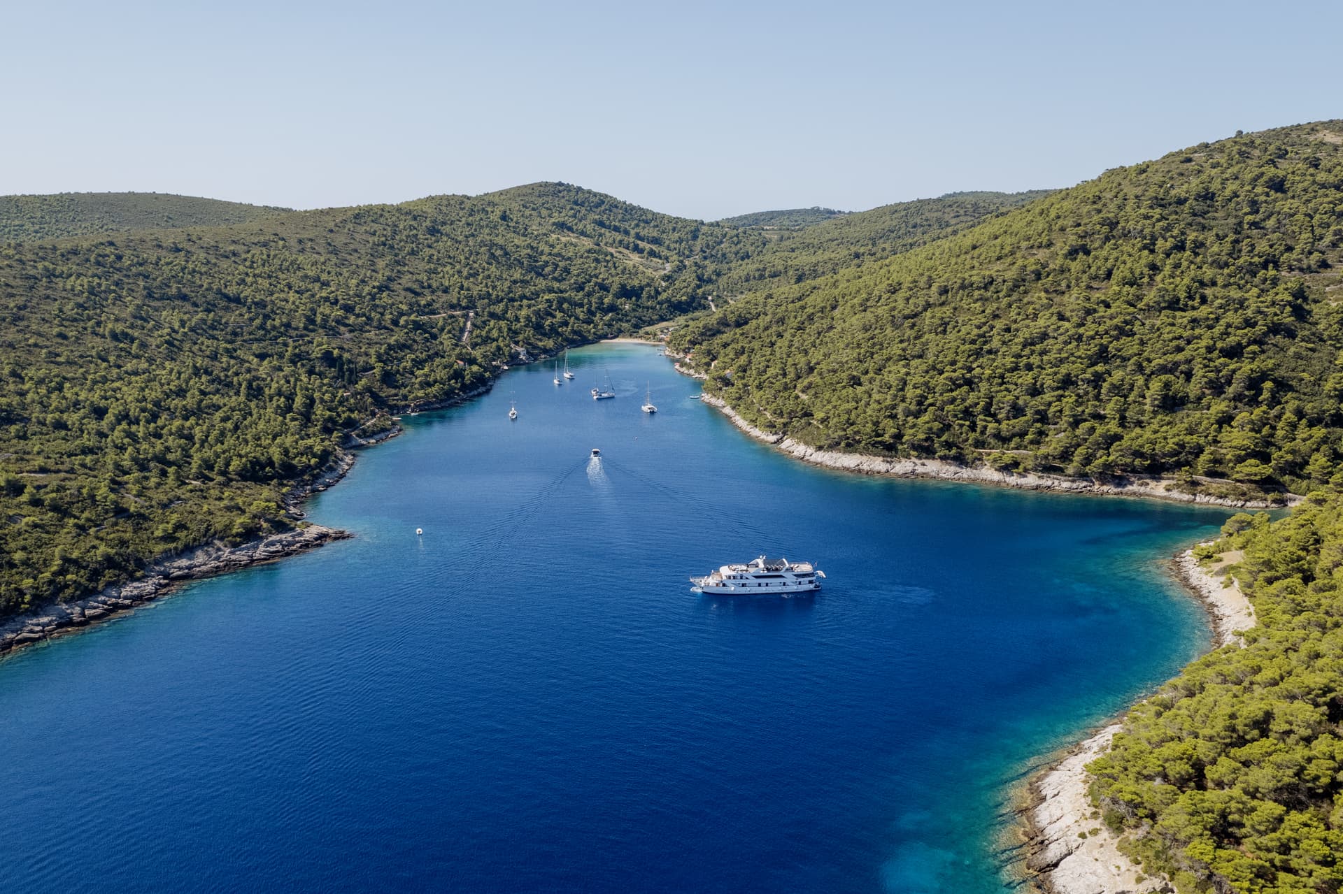 Yacht anchored in a blue coastal bay surrounded by green forested hills