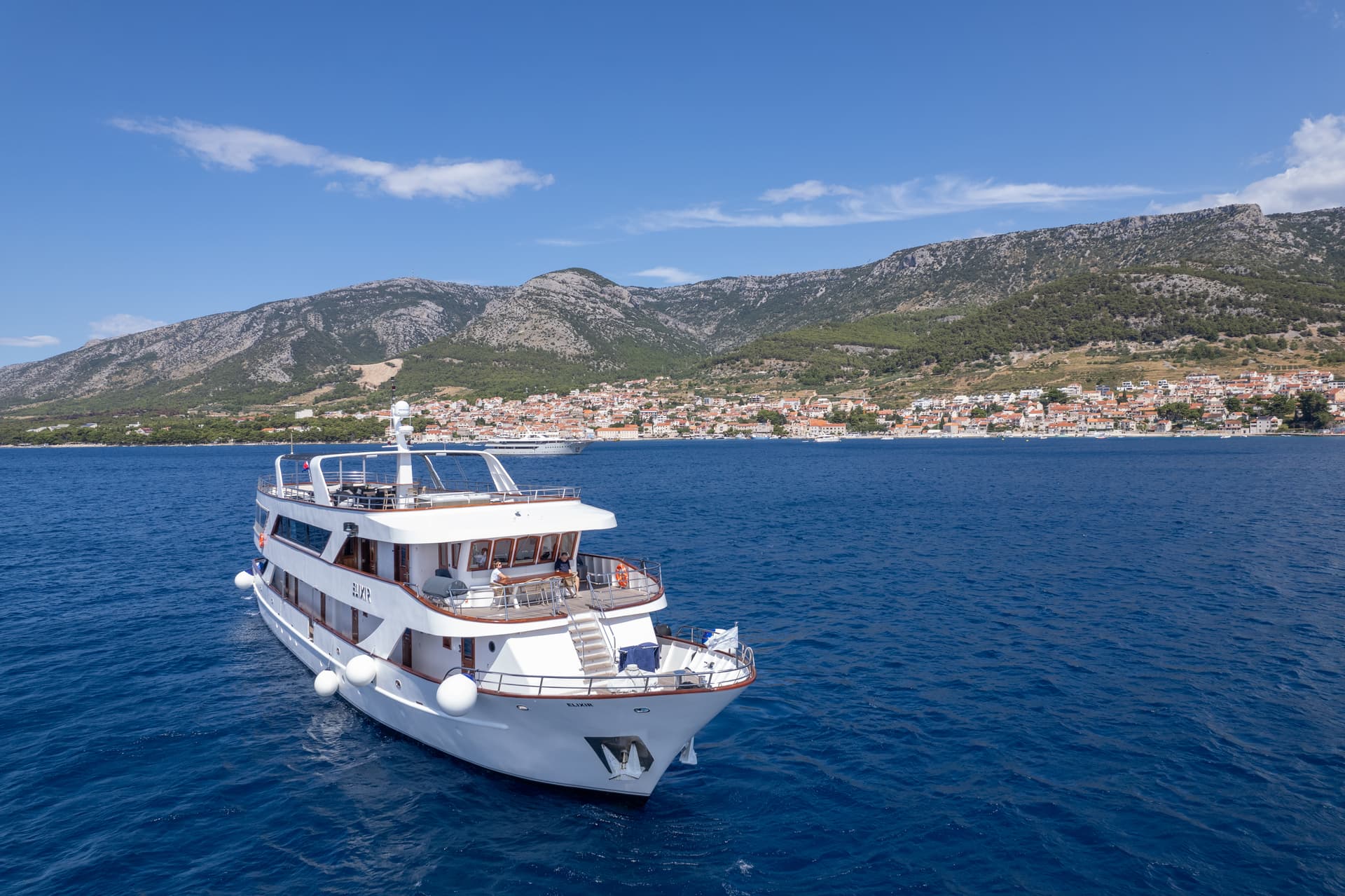 White yacht on blue sea with coastal town and mountains in background
