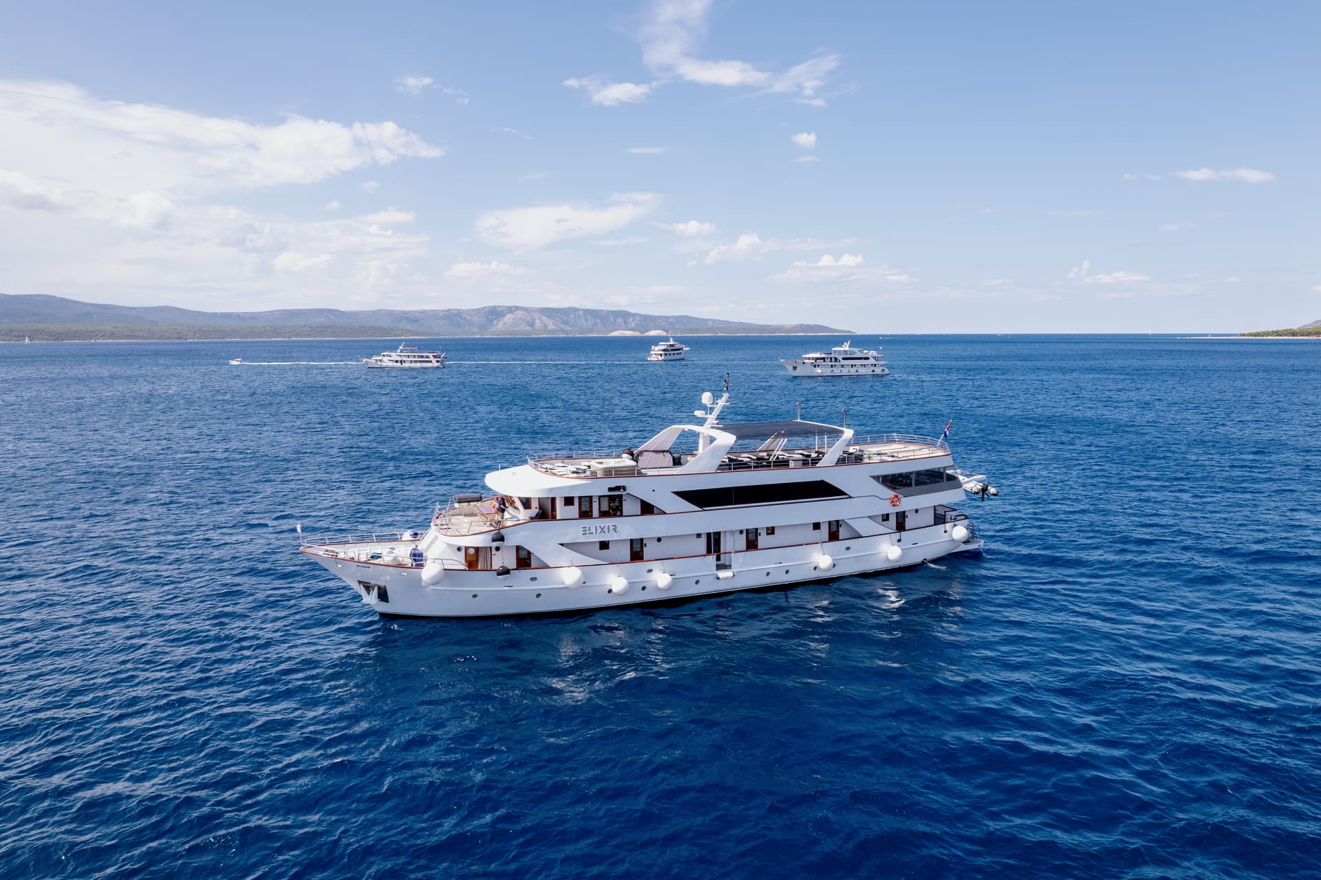 White yacht cruising on blue sea with other boats in the distance