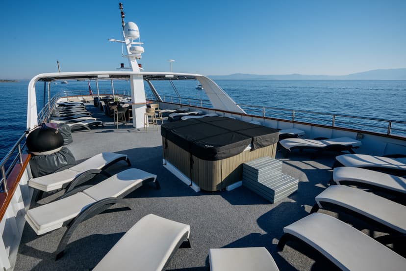 Yacht deck with covered lounge area, hot tub, and sun loungers on blue sea water