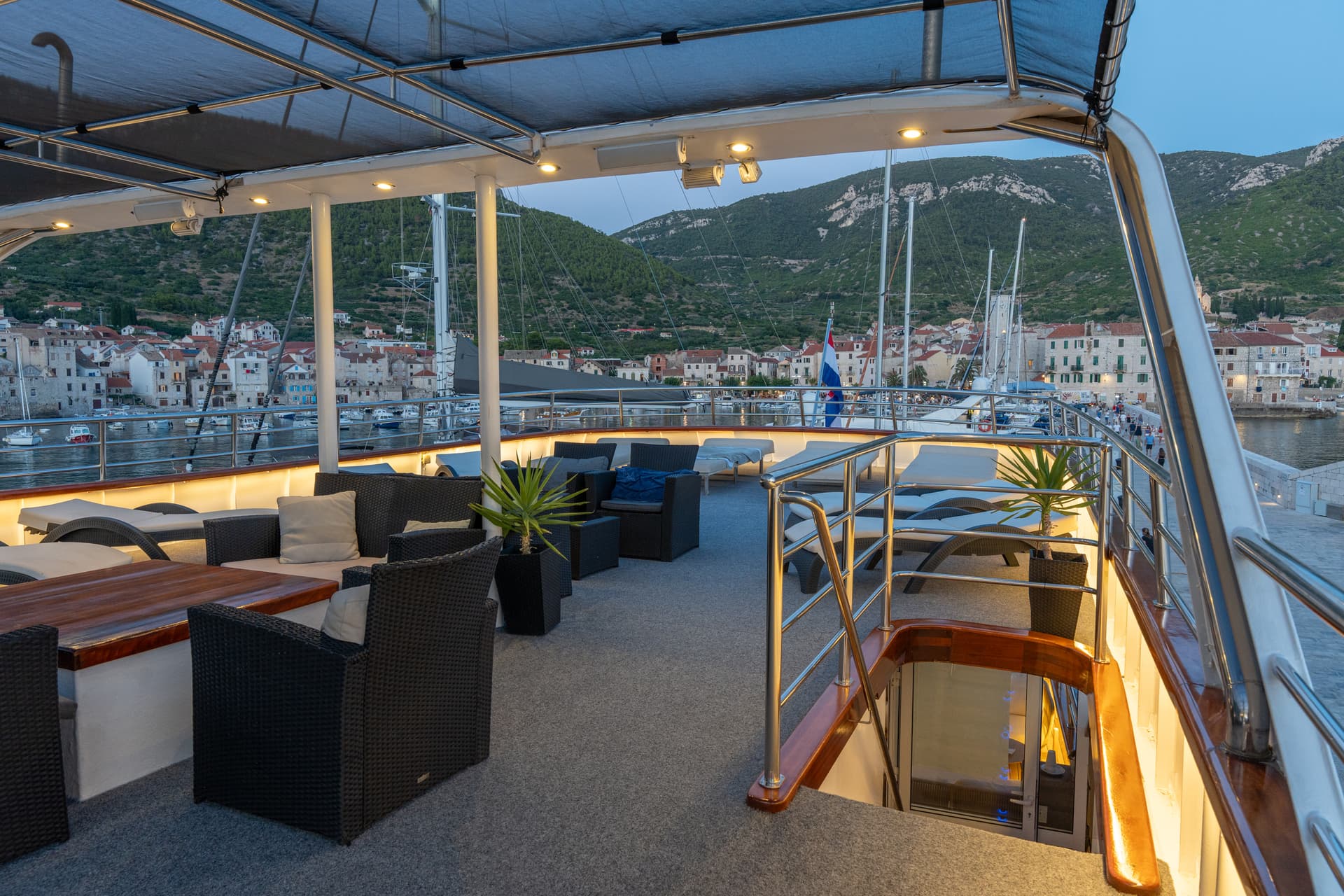 Yacht deck with outdoor seating and lounge chairs overlooking harbor and coastal town