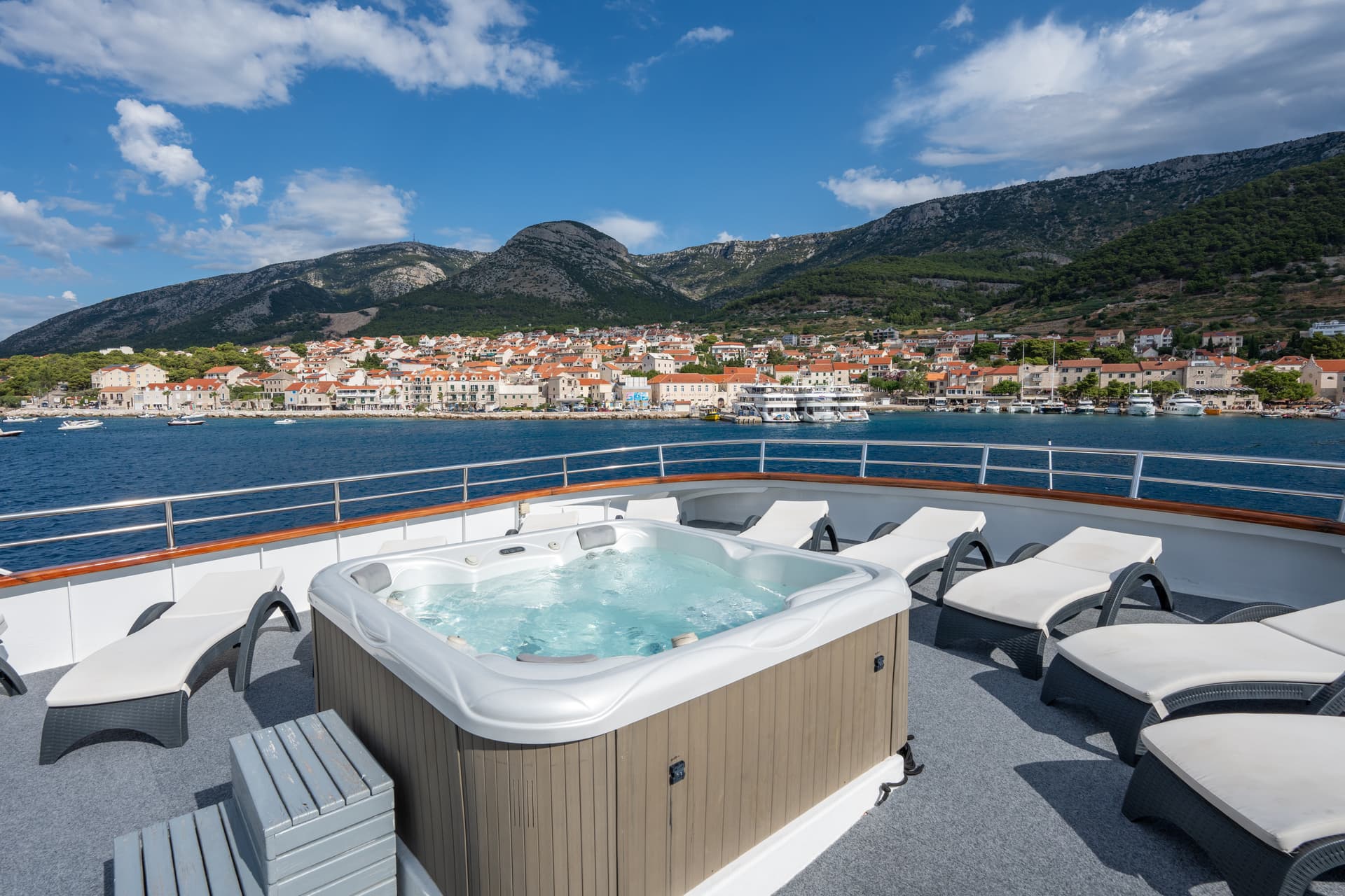 Jacuzzi hot tub and sun loungers on a yacht deck overlooking a coastal town and mountains