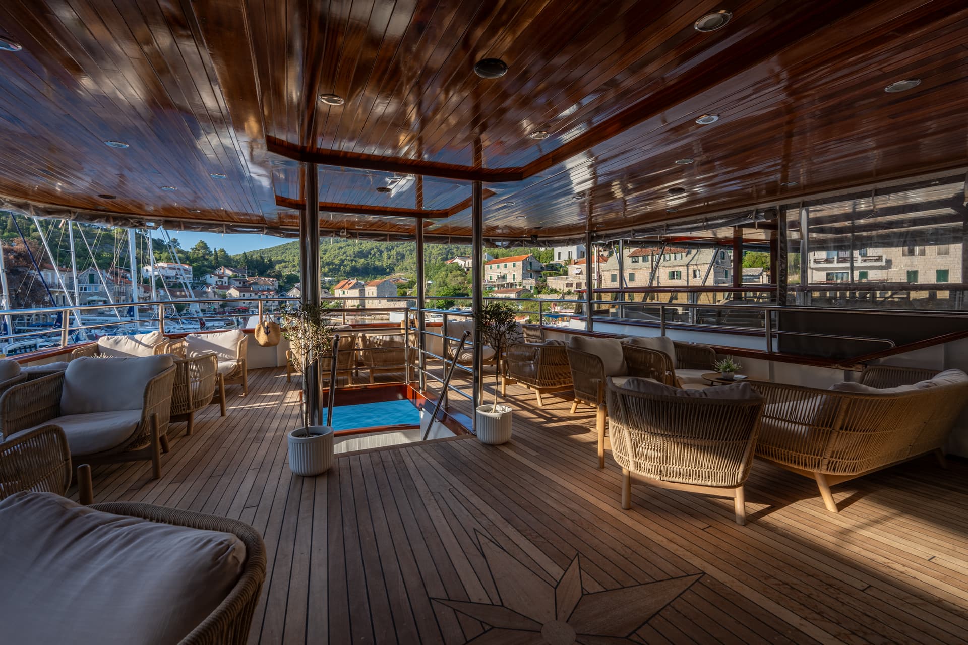 Luxury yacht deck lounge with wooden flooring and comfortable seating facing a harbor view