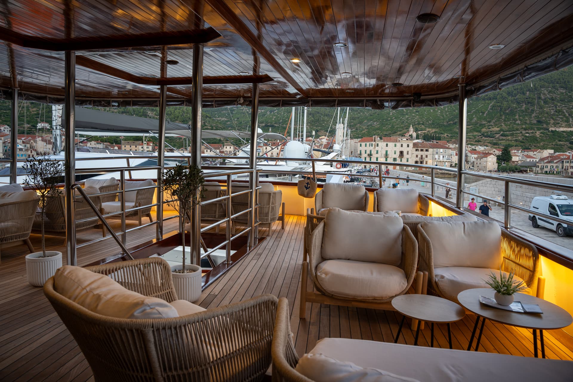 Yacht deck lounge with comfortable armchairs and wooden flooring overlooking a harbor town