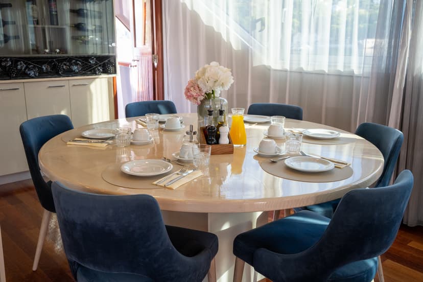 Round dining table set with white plates, glasses, and blue upholstered chairs inside a room
