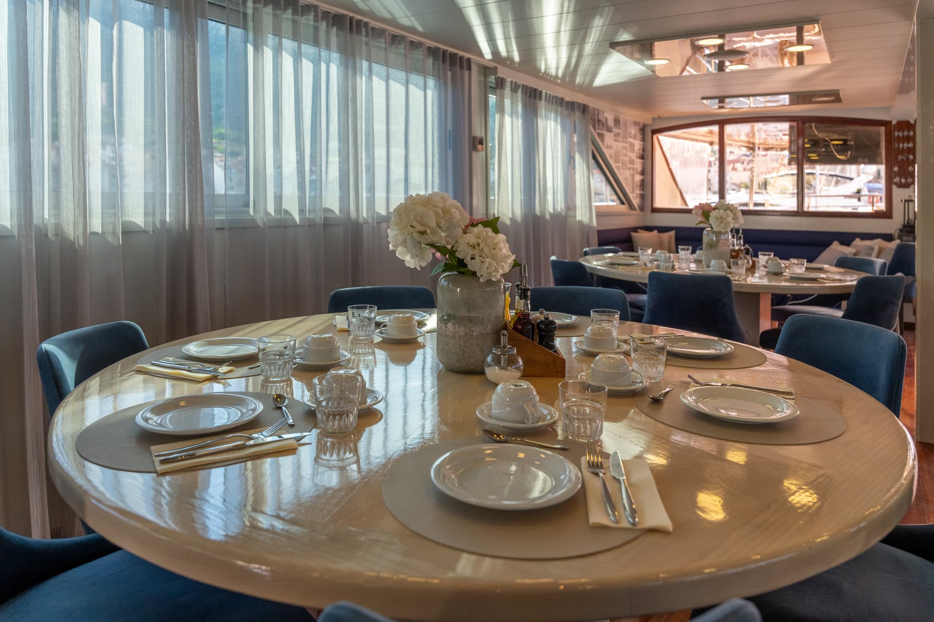 Round dining tables set with plates, cups, and glasses inside a modern boat interior