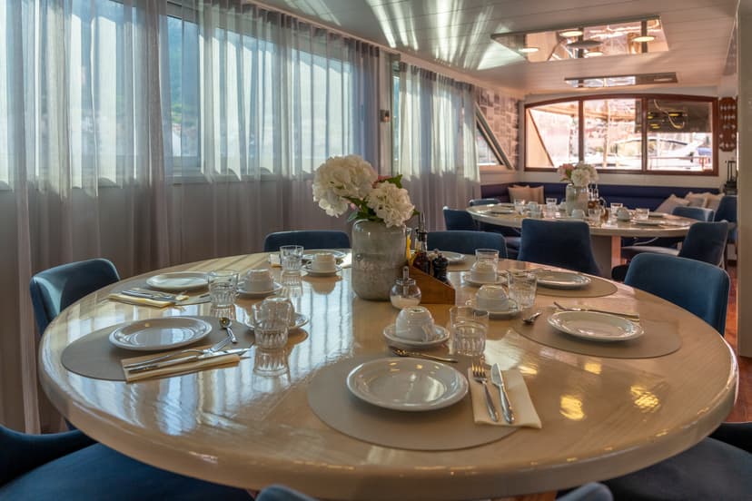 Round dining tables set with plates, cups, and glasses inside a modern boat interior