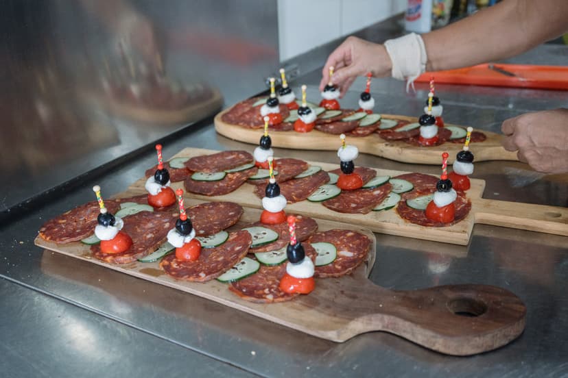 Preparing tapas appetizers with cured meat, cucumber, tomato, cheese, and olives on wooden boards