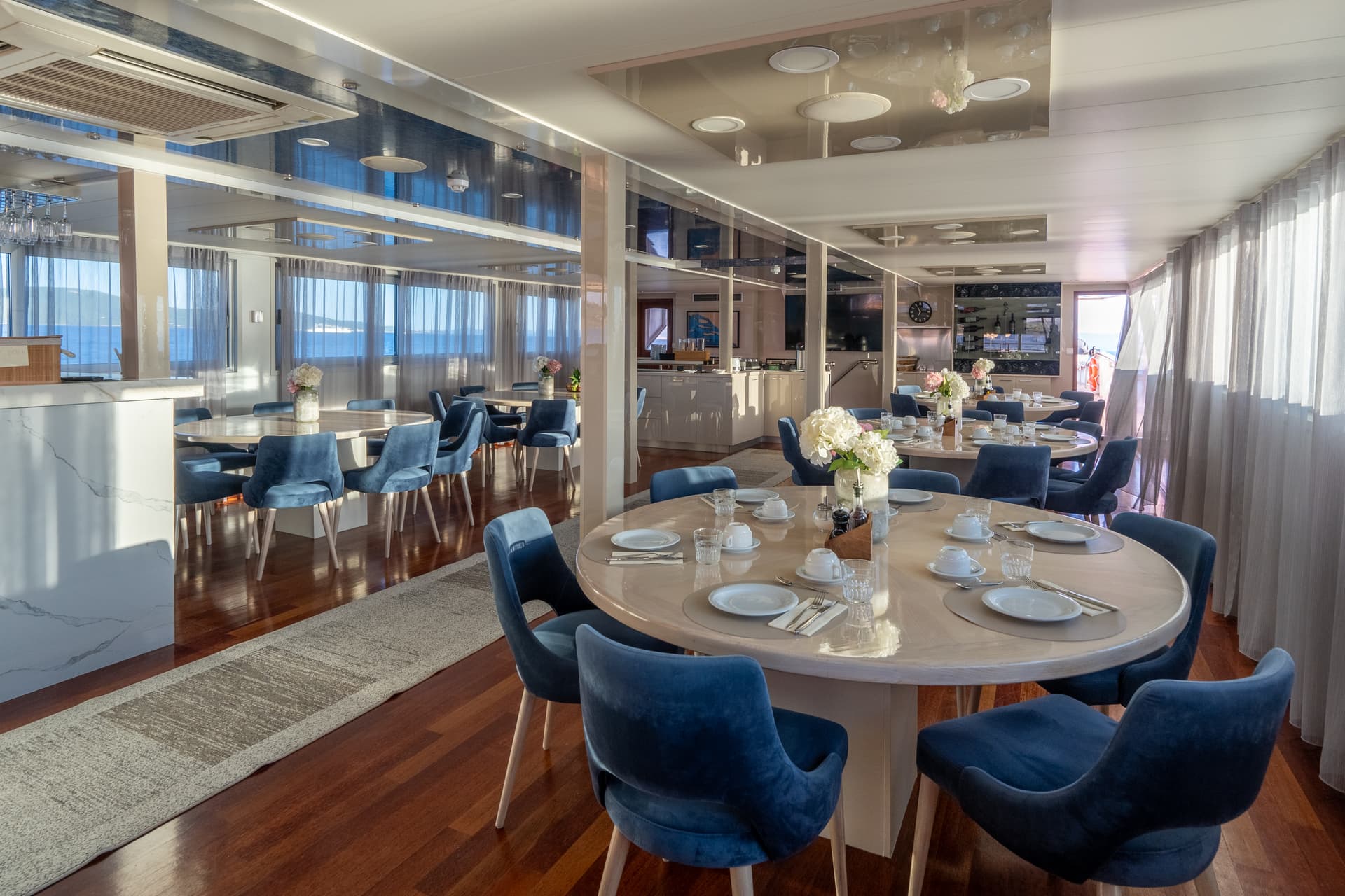 Modern ship dining room with round tables and blue velvet chairs overlooking the sea