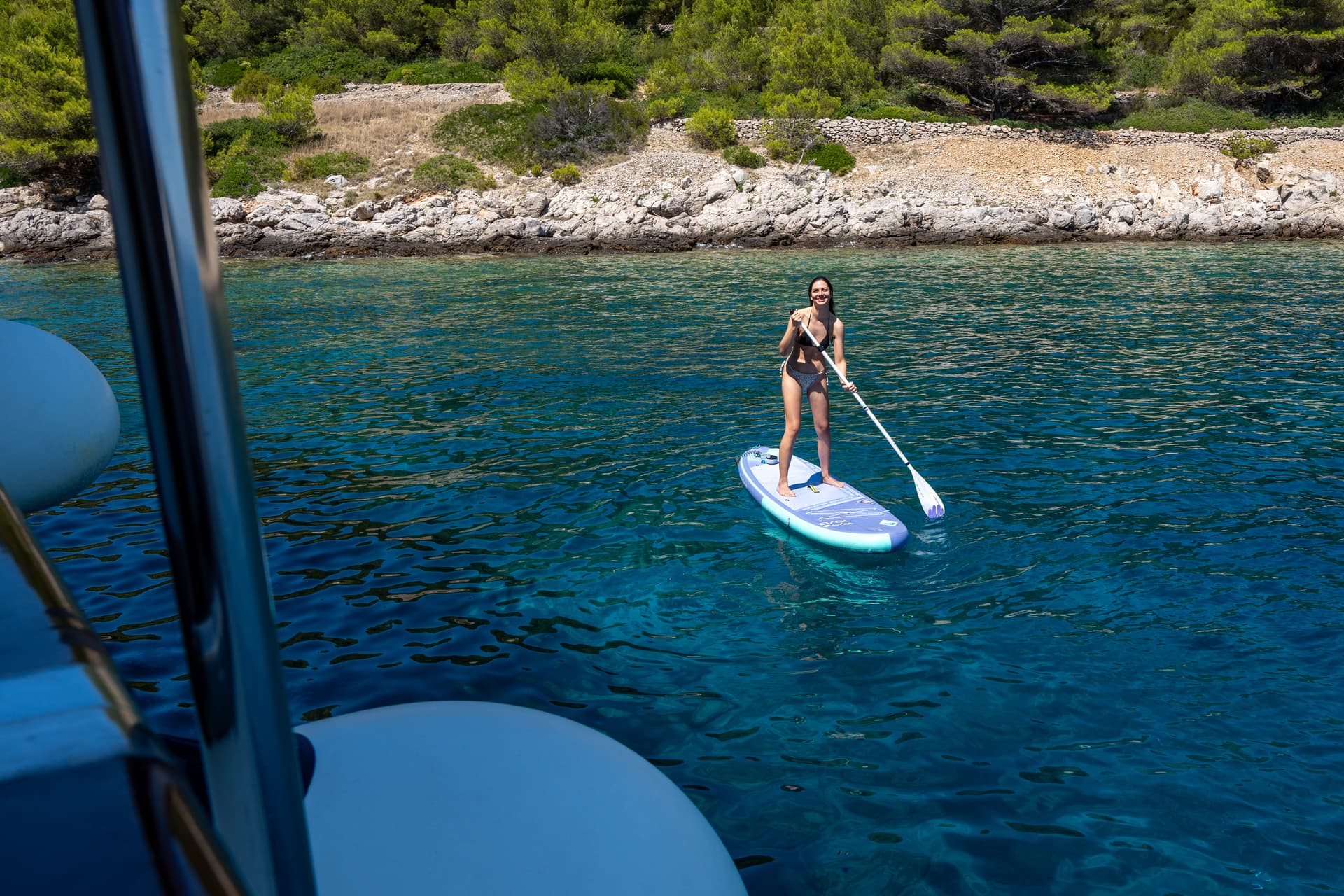 Person stand up paddleboarding on clear blue coastal waters near a rocky shore
