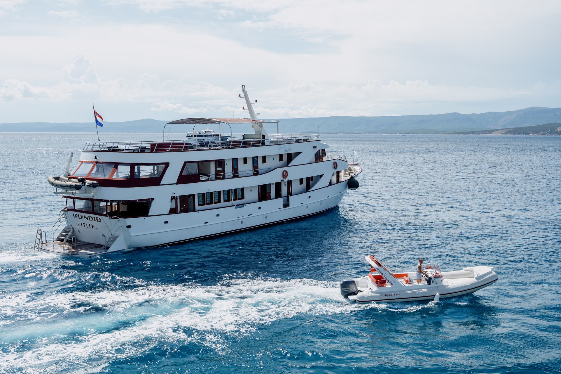Large yacht and small motorboat on coastal waters with mountains in the background