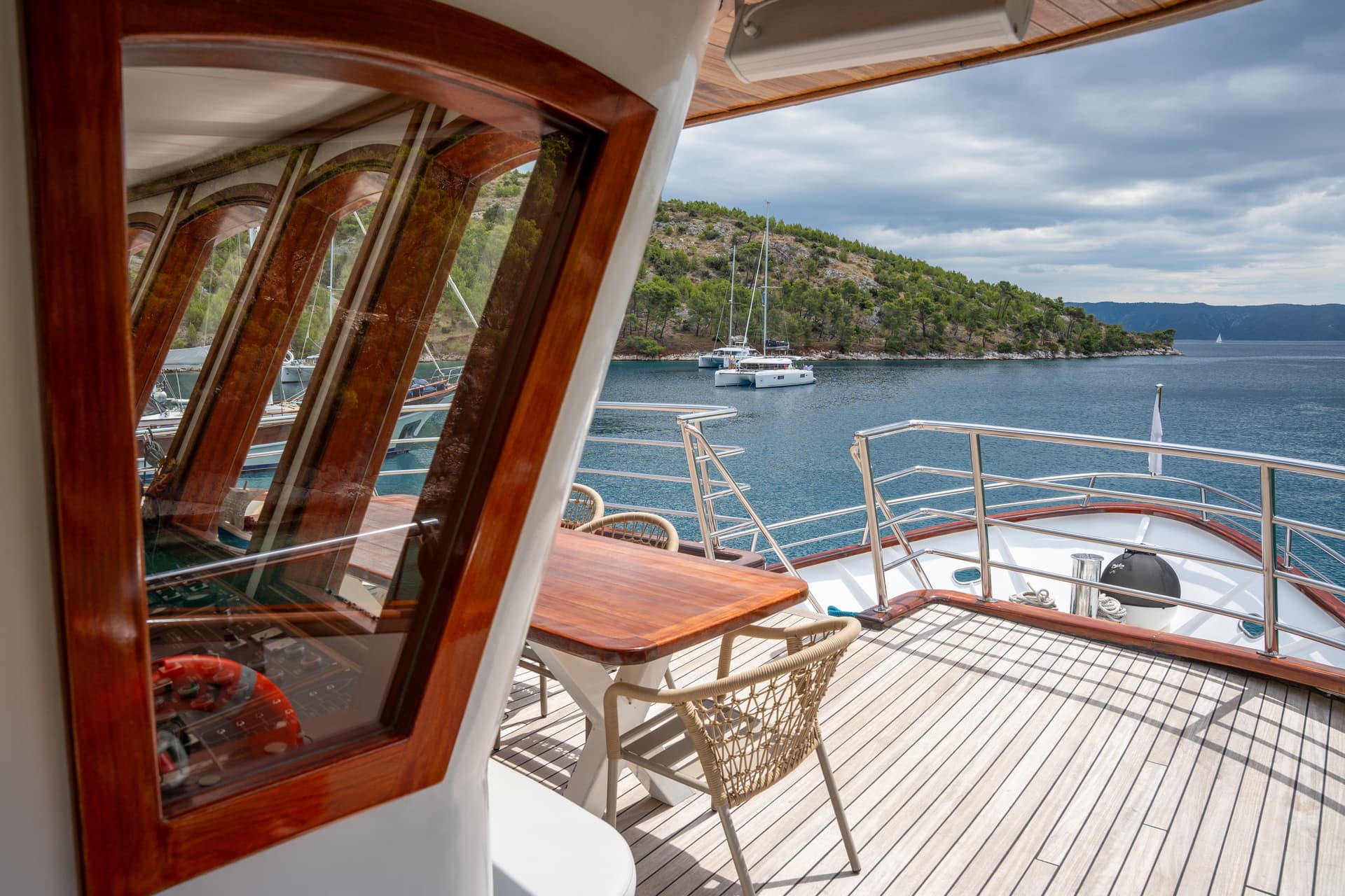 Yacht deck with wooden dining table and chairs overlooking coastal waters and islands
