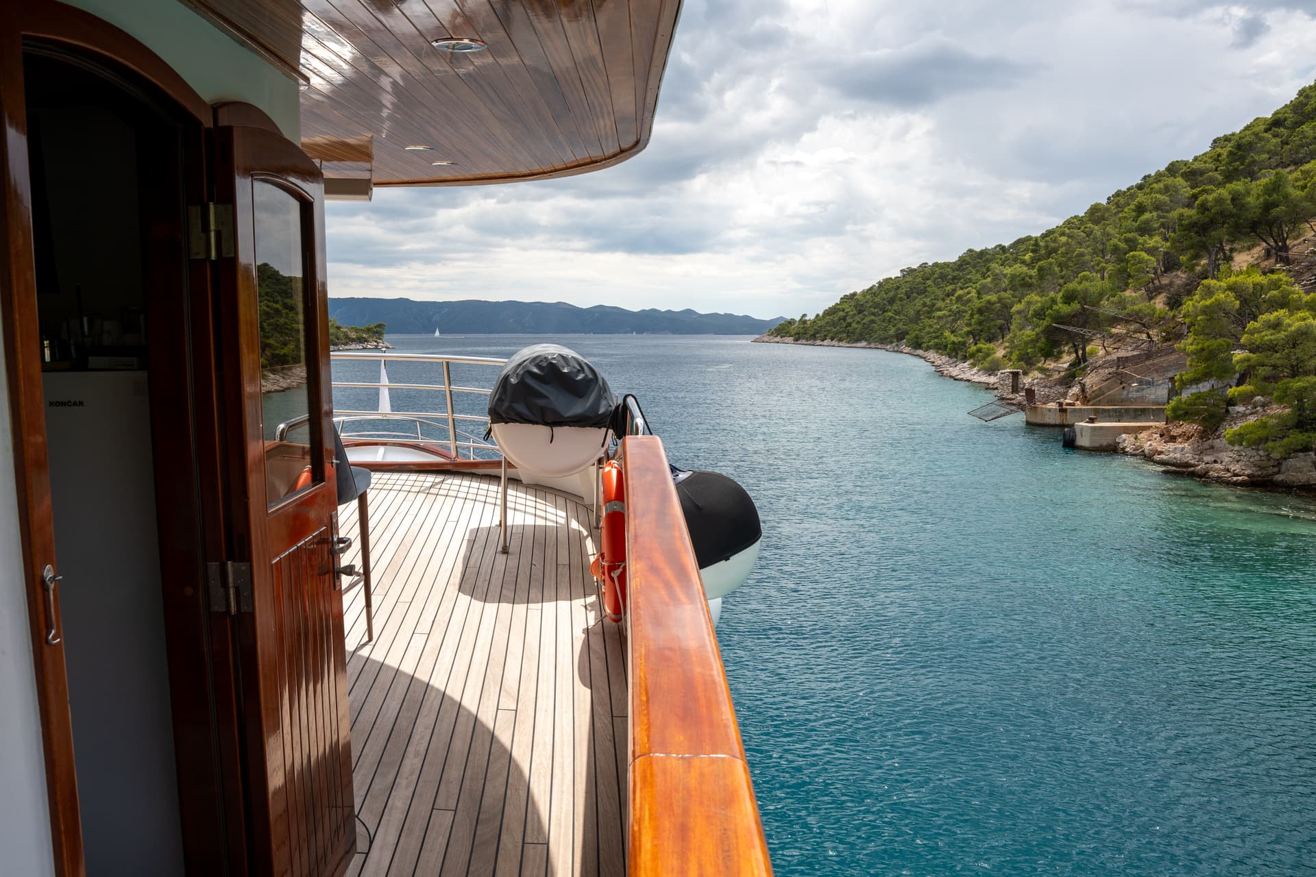 Yacht deck with wooden flooring overlooking a coastal channel with forested hills