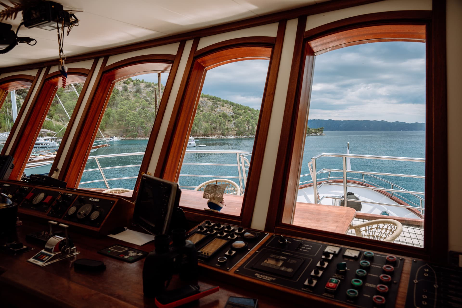 Boat bridge control panel looking out arched windows to coastal waters and wooded hills