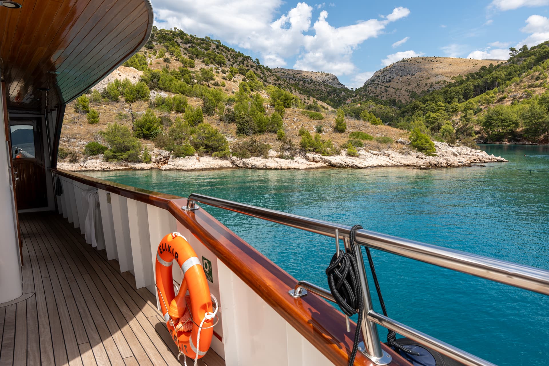 Yacht deck with orange life ring sailing on coastal waters near hills
