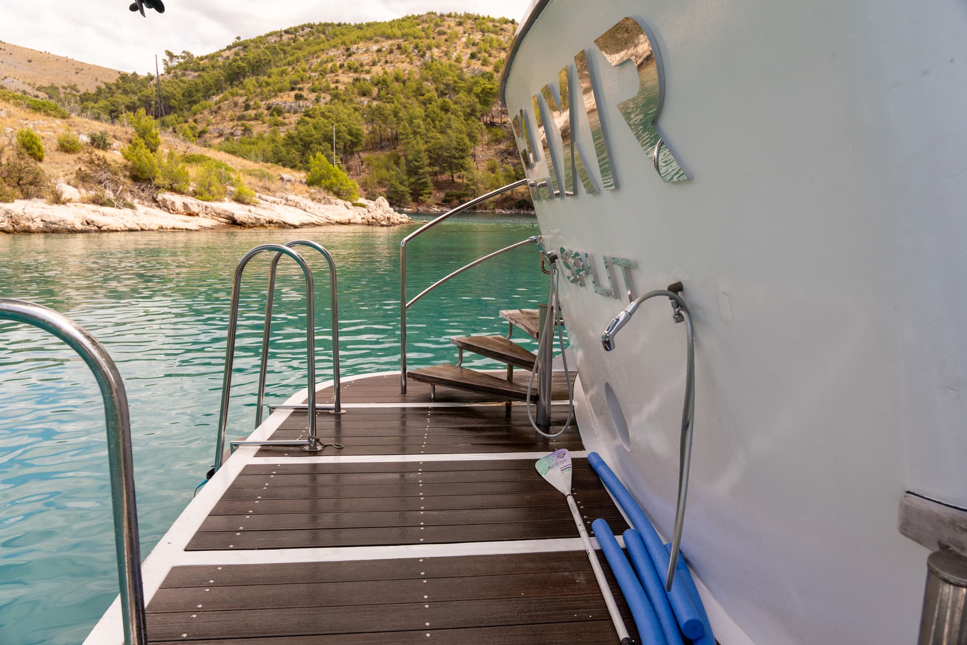Yacht swim platform with wooden deck and stairs anchored in a calm bay
