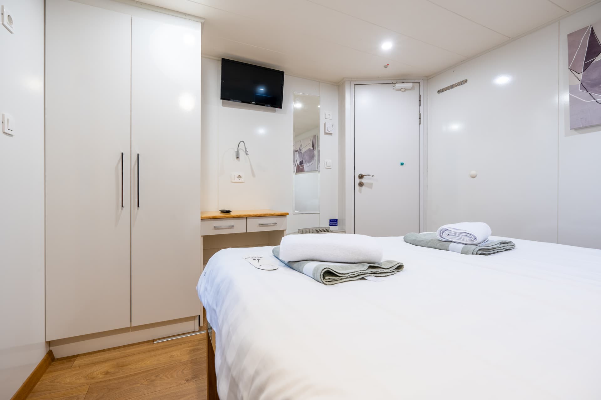 Hotel room interior with white bed linens, towels, wardrobe, and wall-mounted television