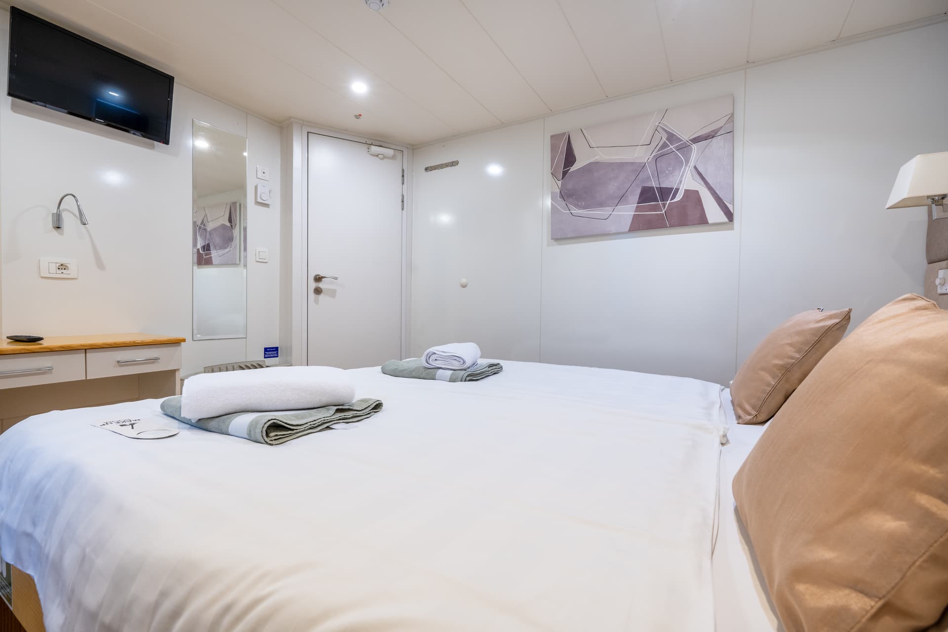 Cruise ship cabin with double bed, TV, and abstract wall art