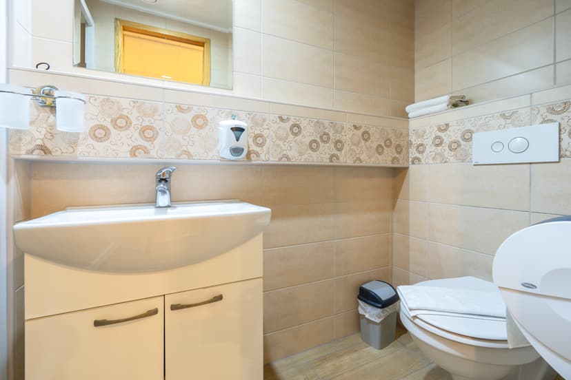 Modern hotel bathroom with beige tiled walls, white sink vanity, and toilet