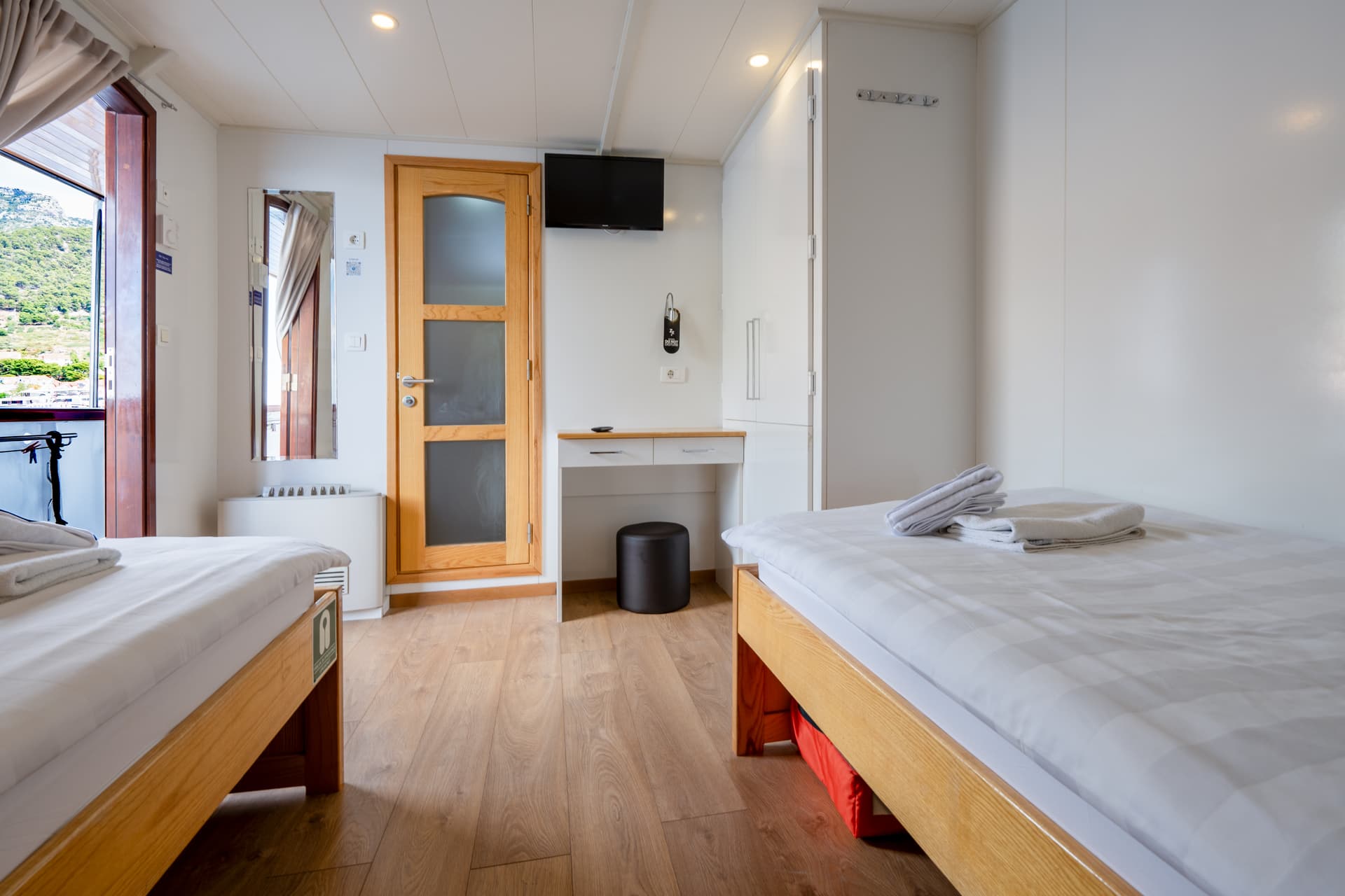 Twin cabin interior on a cruise ship with two beds and wooden flooring