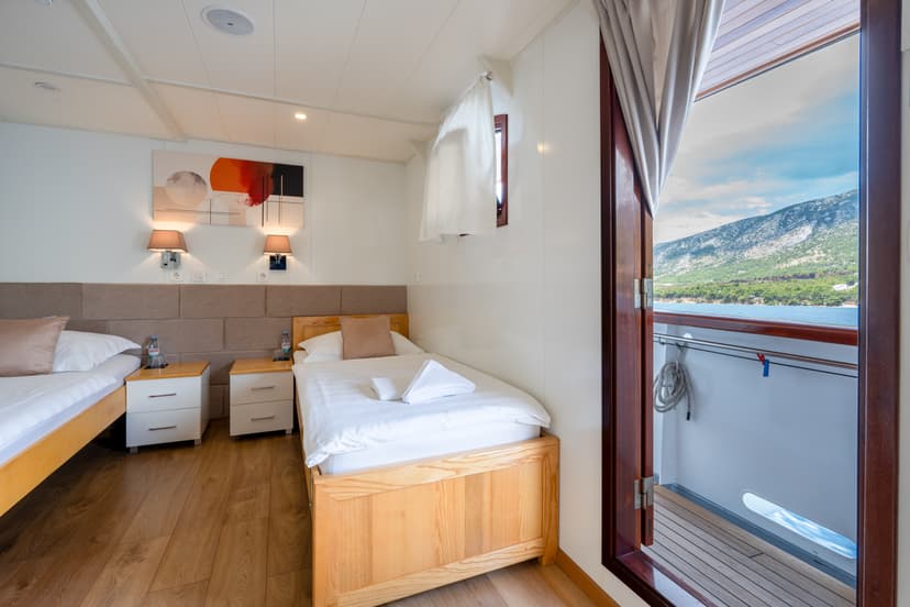 Cruise ship cabin with twin beds and open balcony door overlooking coastal mountains