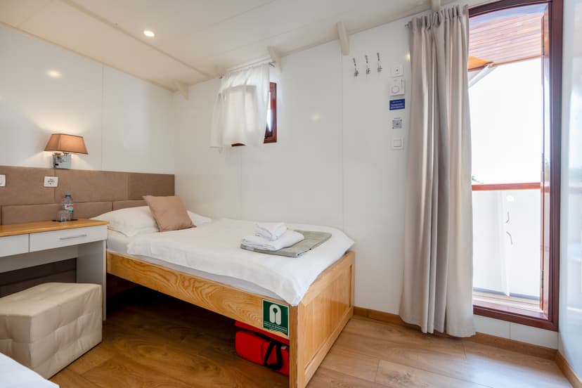 Single cabin interior with wooden bed, white linens, desk, and doorway leading outside