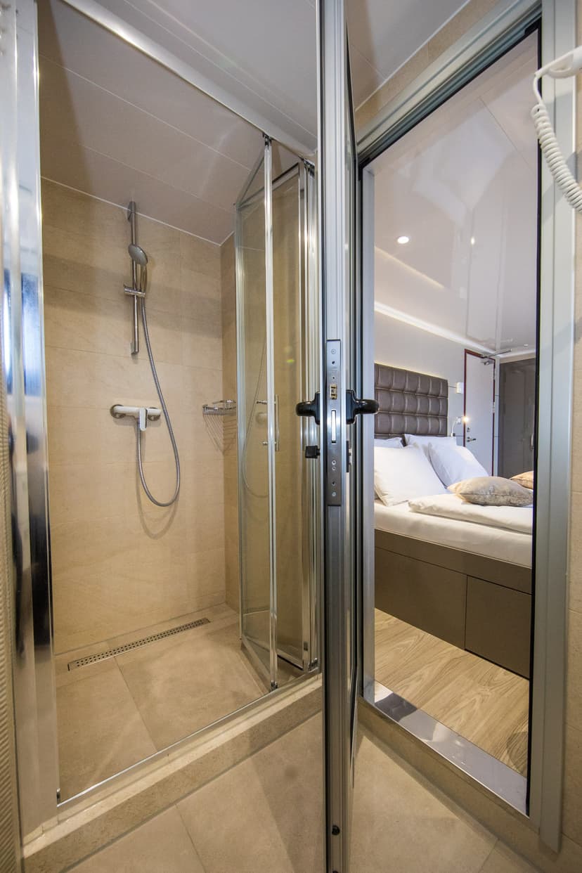 Modern bathroom with glass-enclosed shower stall opening to a bedroom with bed
