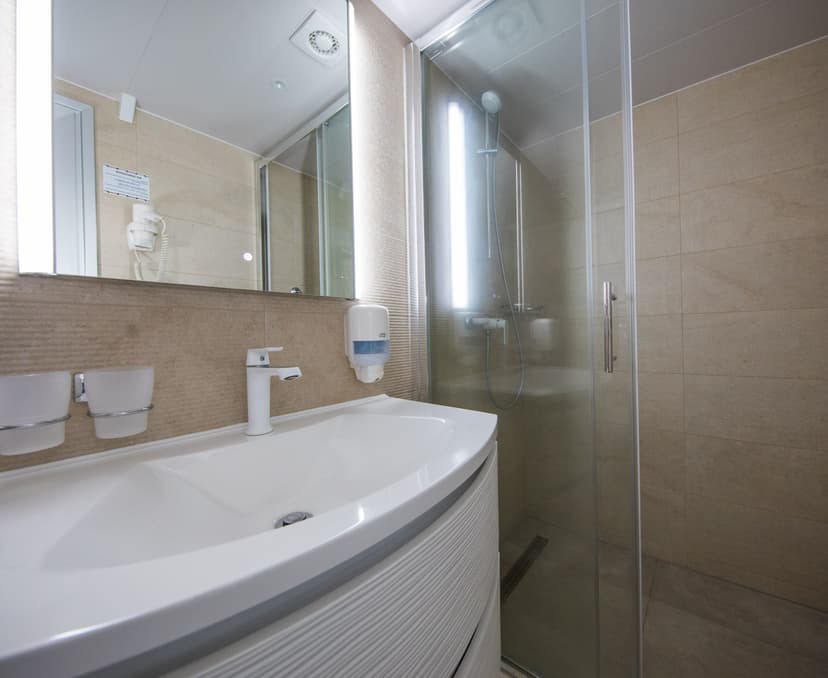 Modern hotel bathroom with white vanity sink, illuminated mirror, and glass shower enclosure