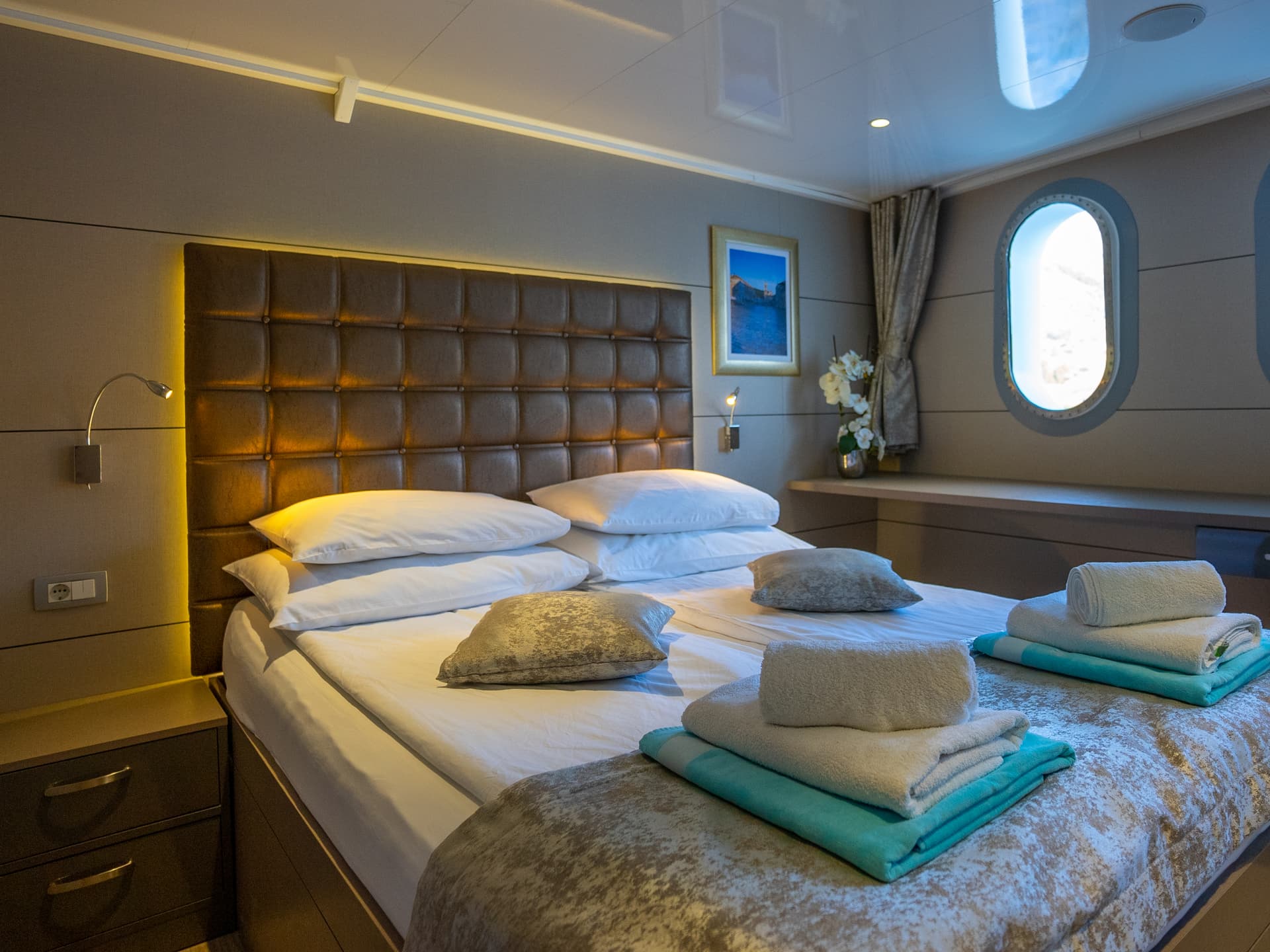 Luxury boat cabin bedroom with double bed, white linens, and porthole window