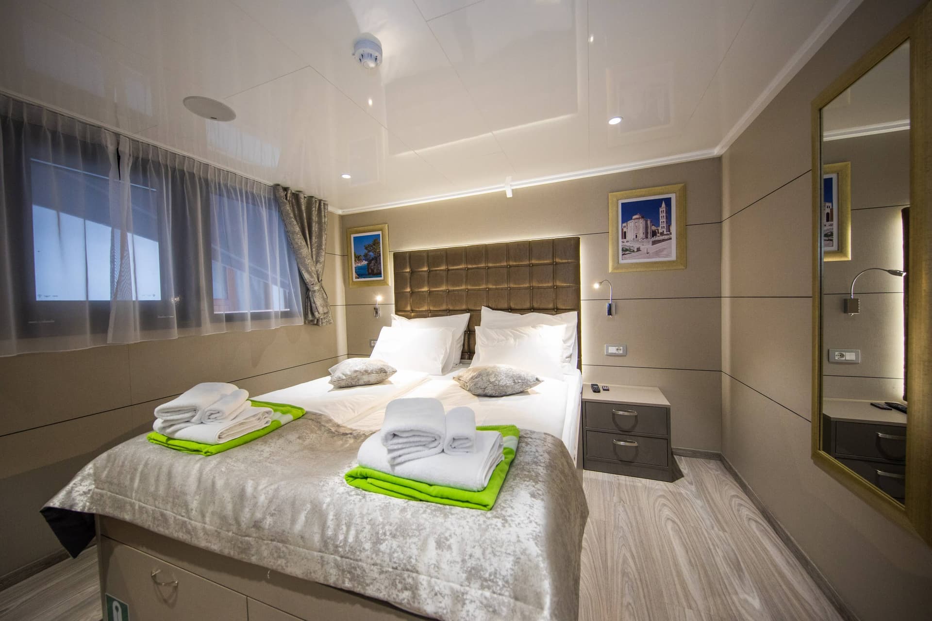 Modern cabin bedroom on main deck with double bed, white linens, folded towels, and framed artwork.