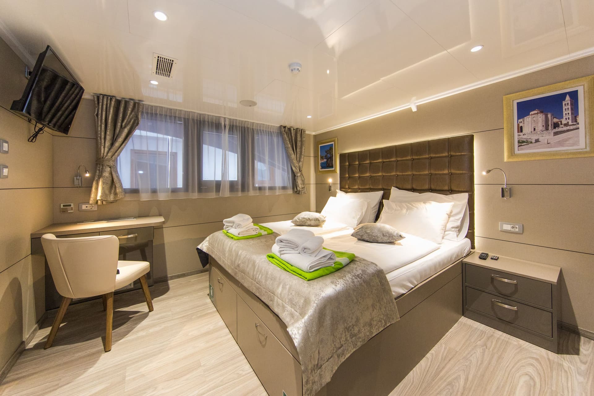 Modern cabin bedroom with double bed, desk, and rolled towels on the main deck of a yacht